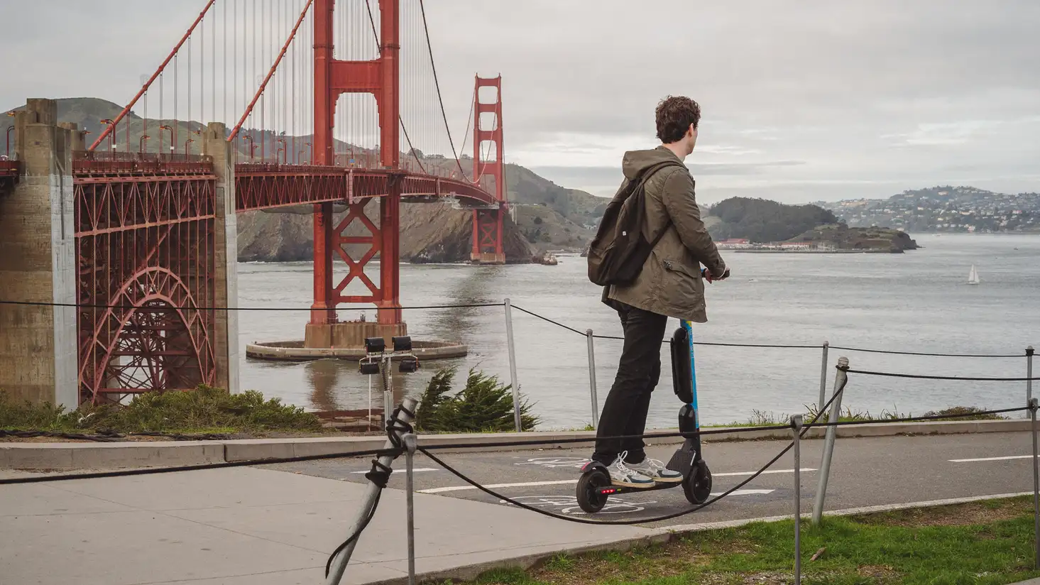 A man riding an electric scooter with the Golden Gate Bridge in the background.